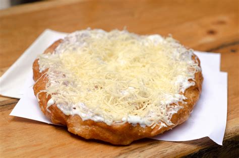Hagyományos piaci lángos friss tejföllel és sajttal meghintve egy fa tálcán