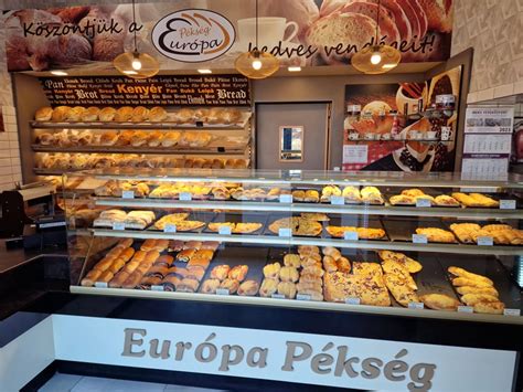 Fotó: Egy pékség dolgozója, aki éppen a frissen sült sós pereceket rendezi el a pultban, a háttérben modern fizetési lehetőségekkel.