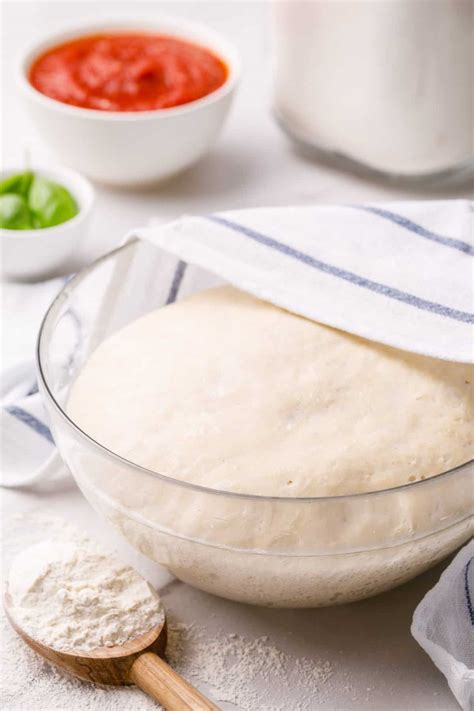 Proofed pizza dough in a bowl covered with a kitchen towel