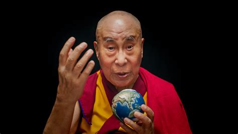 A XIV. Dalai Láma mosolyogva, meditációs pózban, kék-sárga ruhában