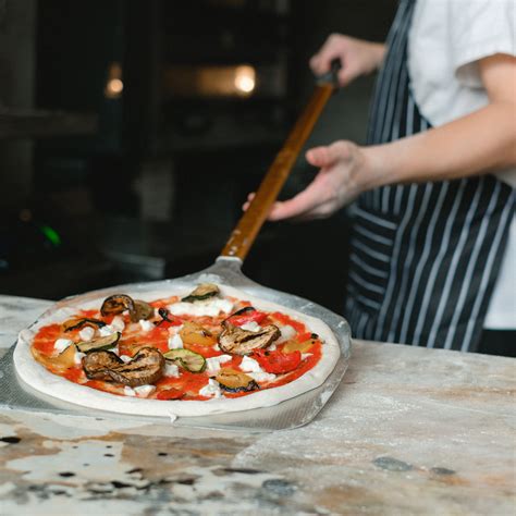 a pizzaiolo éppen a pizzát díszíti friss bazsalikomlevelekkel