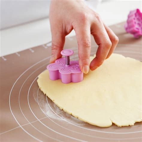 egy nagy méretű, bonyolult mintázatú mézeskalács kiszúró forma, amely mellett már kisült, díszített mézeskalács látható