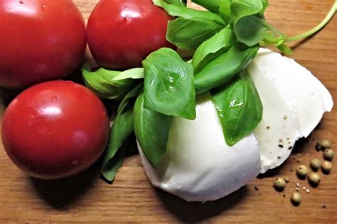 Friss paradicsom, bazsalikom és minőségi mozzarella egy asztalon, előkészítve a pizzakészítéshez
