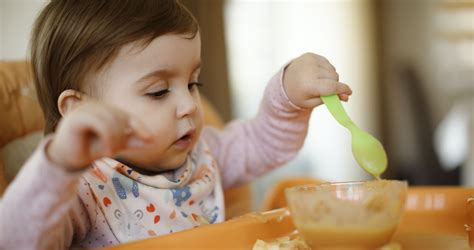 baba, aki önállóan próbálkozik az evéssel, kezében ételdarabkával