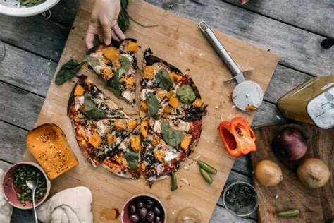 Különböző feltétek tálalva, egy kész pizza mellett